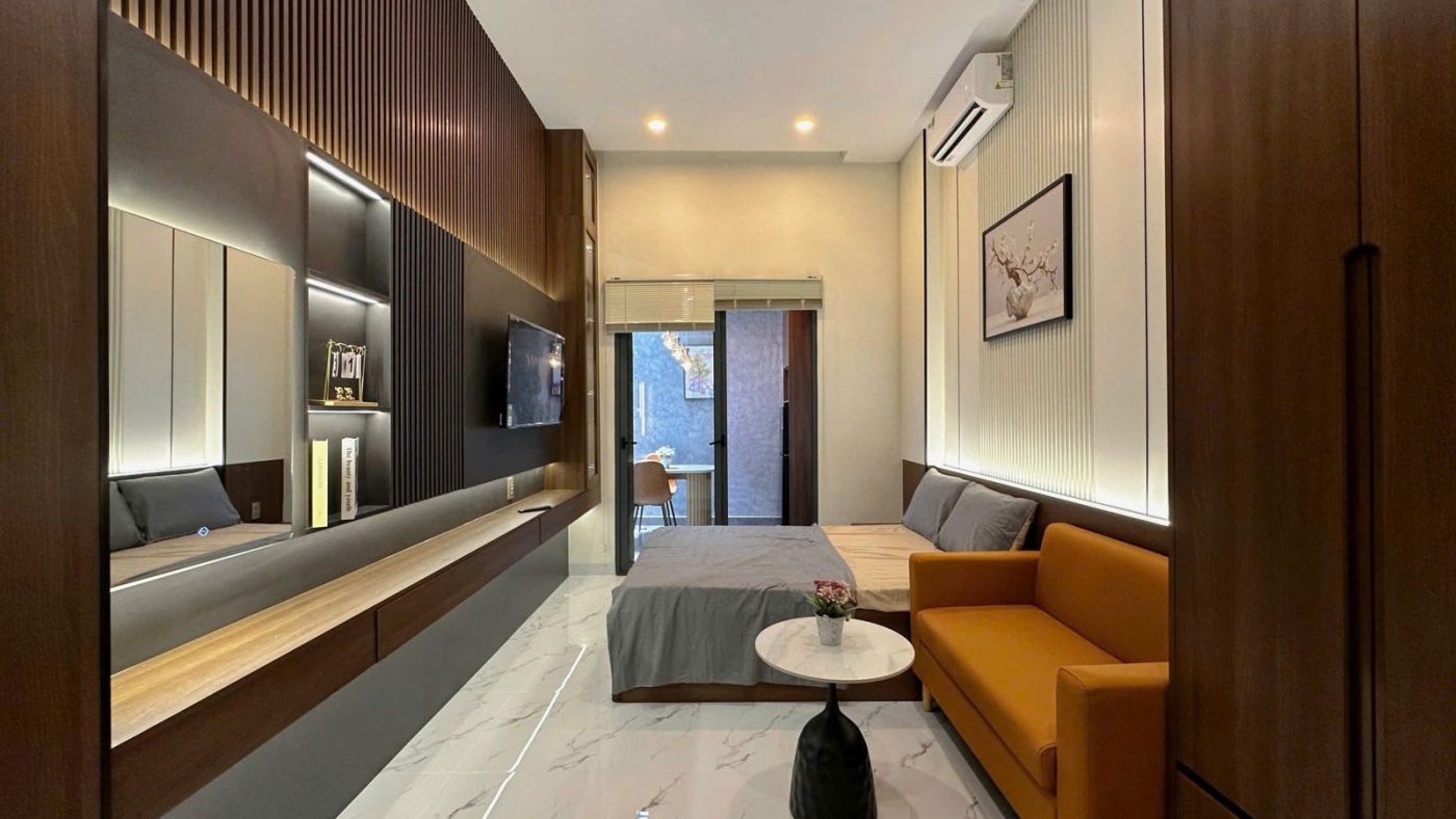 Phòng cho thuê ốp gỗ có sofa cam, giường, tivi và đèn hắt tường, ảnh bìa bài viết về sợ mua hớ nhà đất