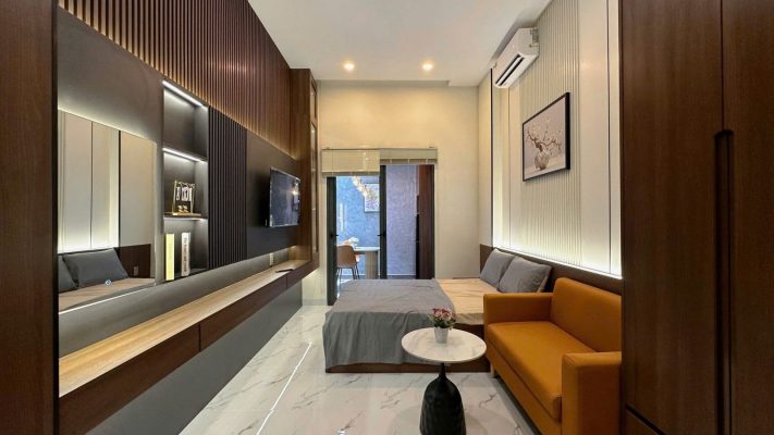 Phòng cho thuê ốp gỗ có sofa cam, giường, tivi và đèn hắt tường, ảnh bìa bài viết về sợ mua hớ nhà đất