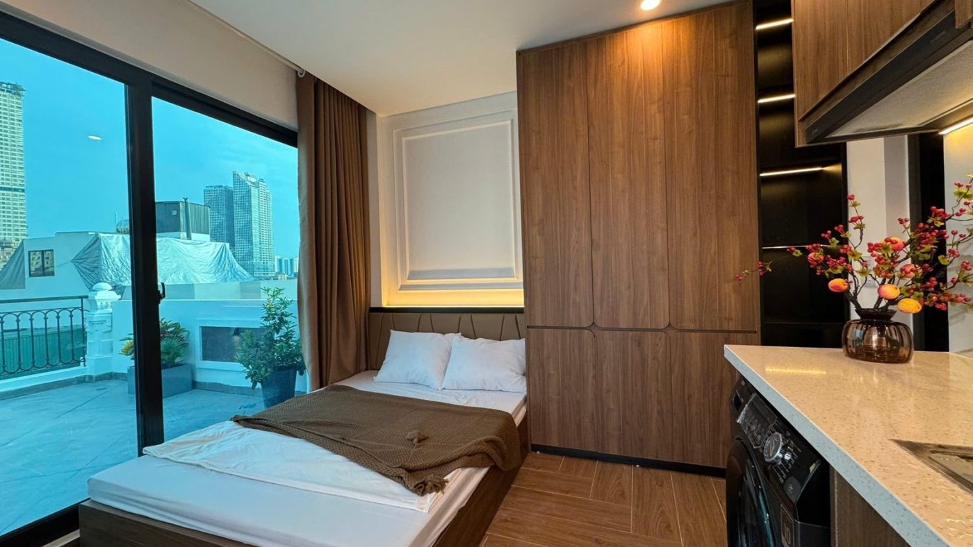 Phòng căn hộ dịch vụ có giường, tủ gỗ và cửa kính lớn nhìn ra thành phố