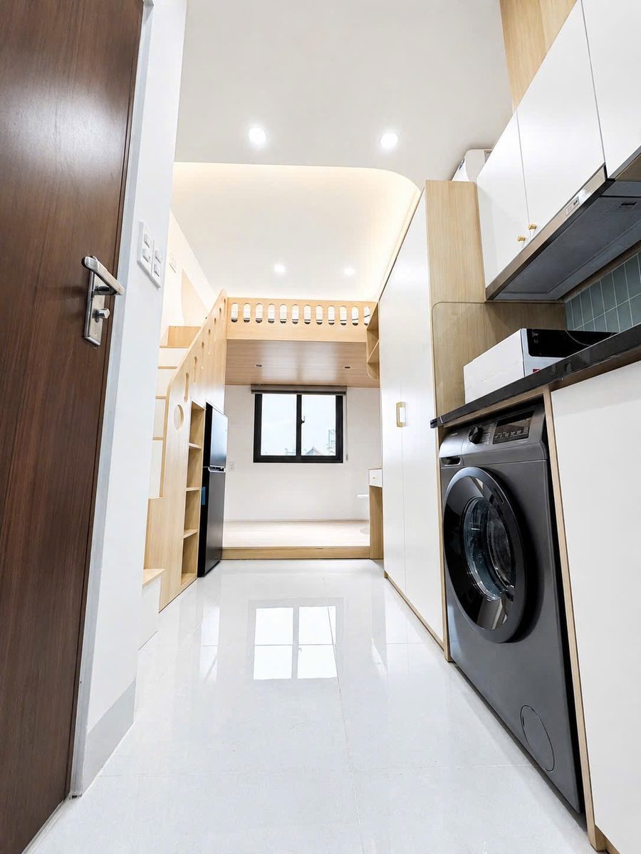 Phòng duplex dài có máy giặt, tủ bếp, sàn gạch trắng và cửa sổ cuối phòng
