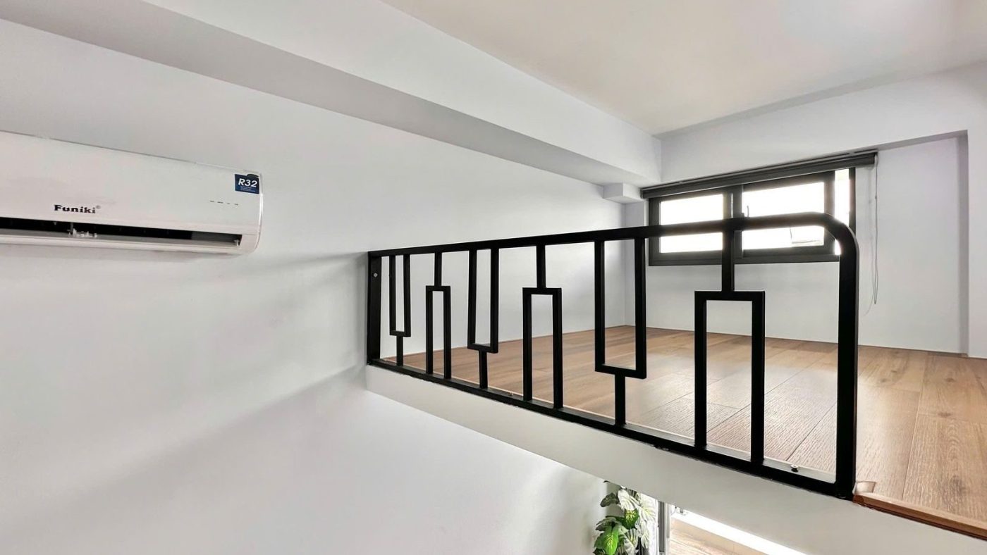 Gác lửng có lan can sắt đen và sàn gỗ trong phòng cho thuê, phía dưới là điều hòa