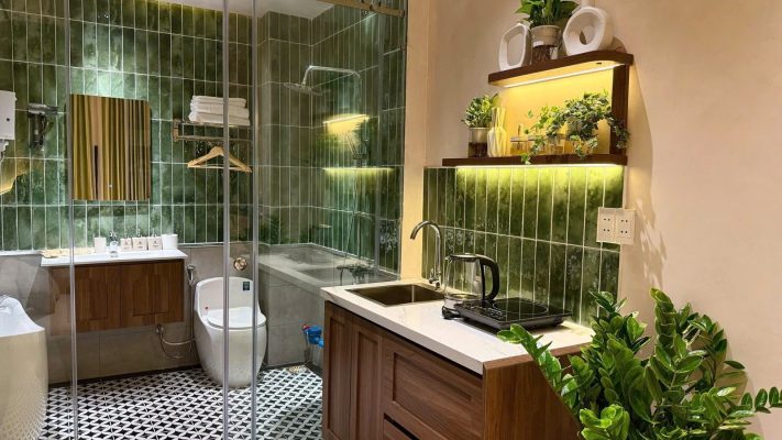 Phòng cho thuê có nhà tắm vách kính ốp gạch xanh, bếp gỗ và kệ cây trang trí