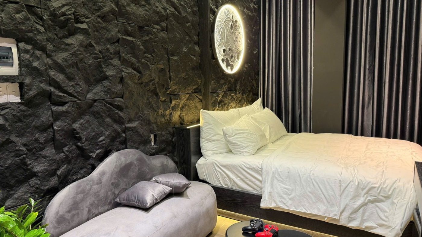 Phòng căn hộ dịch vụ tường ốp đá đen có giường trắng, sofa xám và đèn tròn