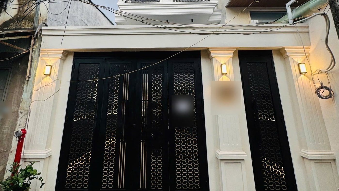 Mặt tiền tầng trệt một tòa nhà cho thuê với cửa sắt đen hoa văn và đèn hắt tường