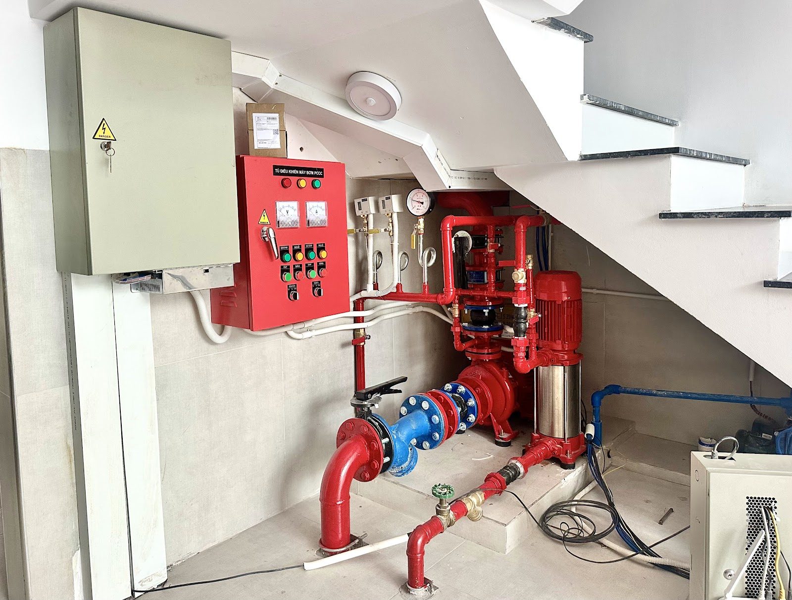 Tủ điều khiển và cụm máy bơm chữa cháy sơn đỏ đặt dưới gầm cầu thang