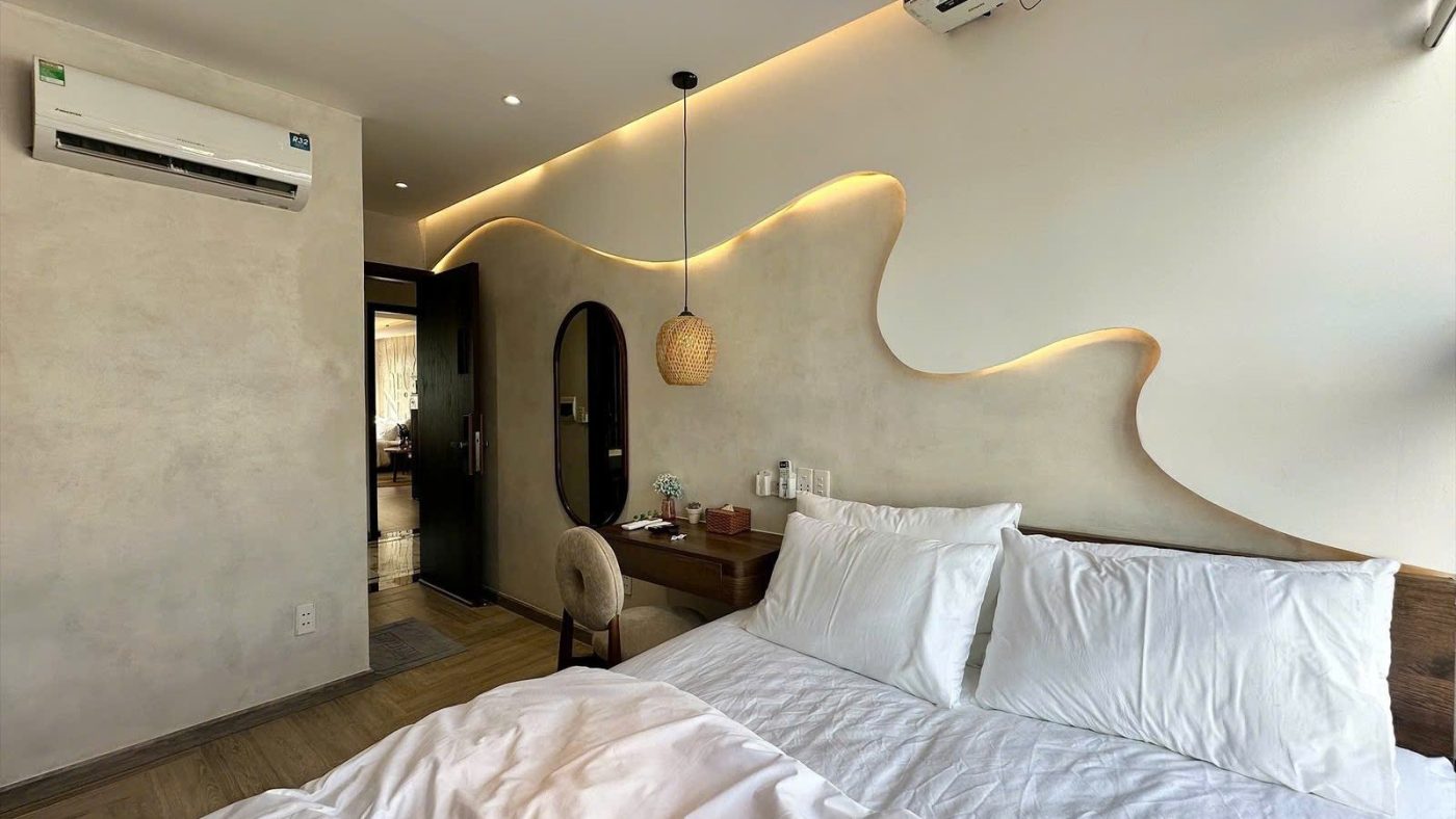 Giường ga trắng trong phòng cho thuê có mảng tường uốn lượn gắn đèn, đèn thả mây và điều hòa