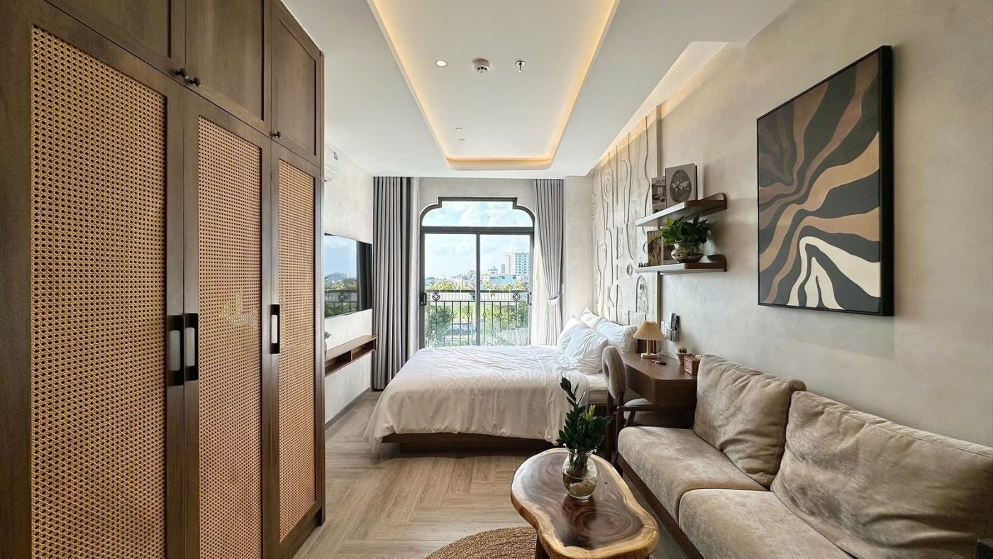 Phòng cho thuê có tủ gỗ cánh mây kịch trần, sofa, bàn trà gỗ và giường cạnh cửa sổ vòm, ảnh bìa bài viết về vay 70% mua nhà