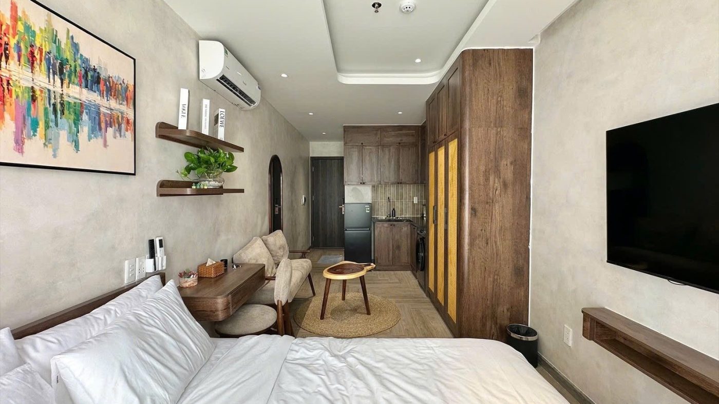 Phòng cho thuê có tranh nhiều màu treo đầu giường, tivi treo tường, tủ áo gỗ và sofa cuối phòng