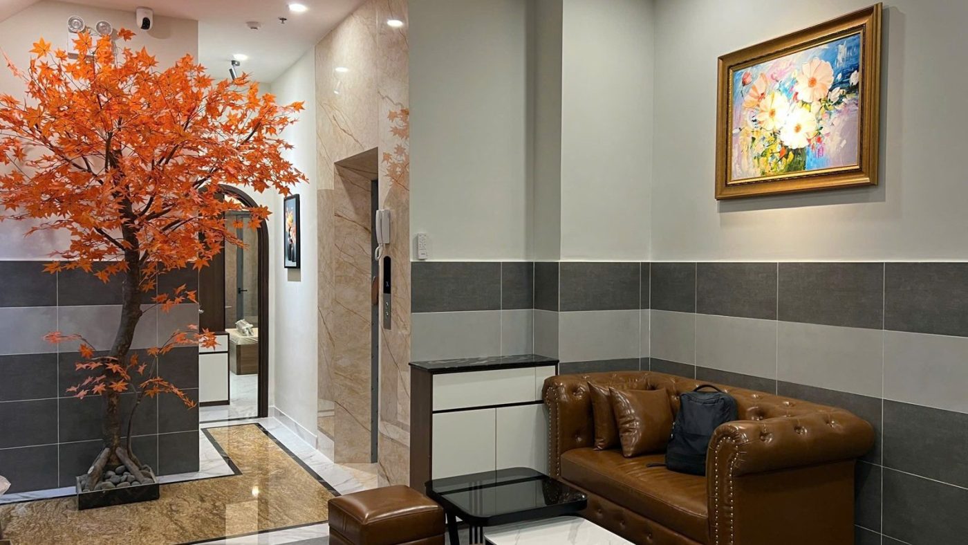 Sảnh nhỏ có cây phong lá cam, ghế sofa da, tranh hoa và cửa thang máy phía sau, ảnh bìa bài viết về vợ chồng vay mua nhà