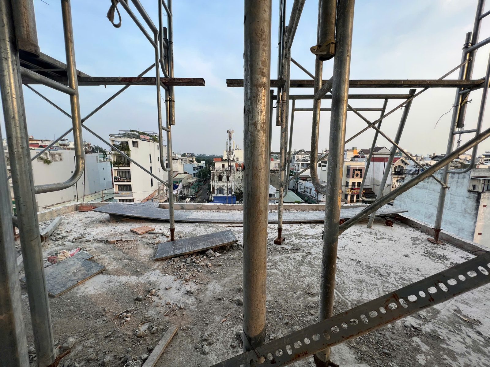 Sàn bê tông một công trình đang xây còn cây chống thép, nhìn ra các nhà cao thấp xung quanh